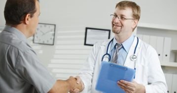 Medical office - middle-aged male doctor greeting patient, shaking hands.